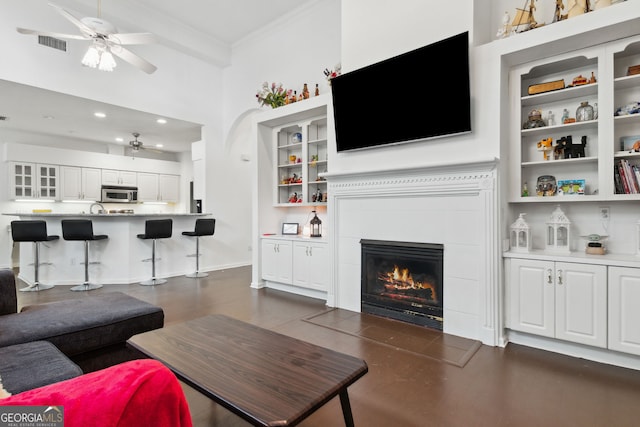 living room with dark hardwood / wood-style floors, built in features, a fireplace, ceiling fan, and crown molding