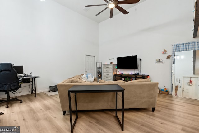 living room with a high ceiling, ceiling fan, and light hardwood / wood-style floors