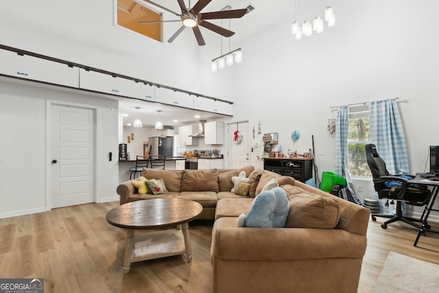 living room with a high ceiling, ceiling fan, and light hardwood / wood-style floors