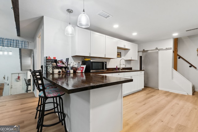 kitchen with sink, white cabinets, a kitchen breakfast bar, hanging light fixtures, and a barn door