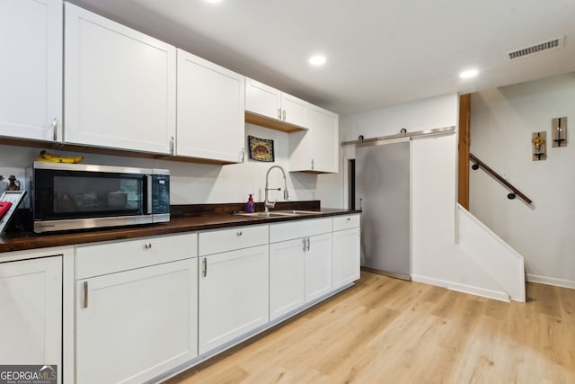 kitchen with a barn door, sink, white cabinets, and light hardwood / wood-style flooring