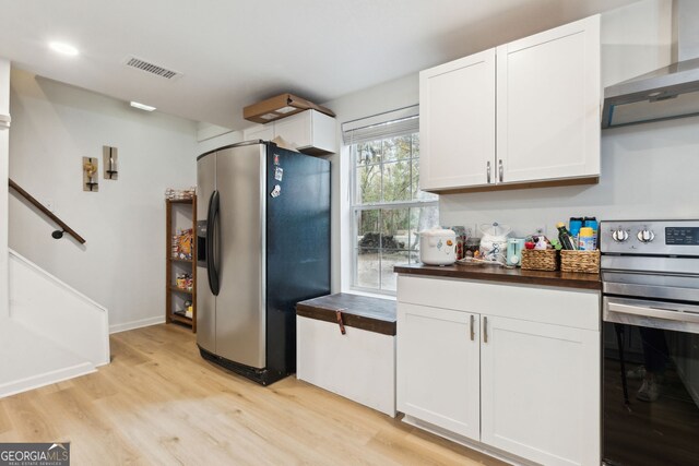 kitchen featuring appliances with stainless steel finishes, white cabinets, light hardwood / wood-style floors, and wall chimney exhaust hood