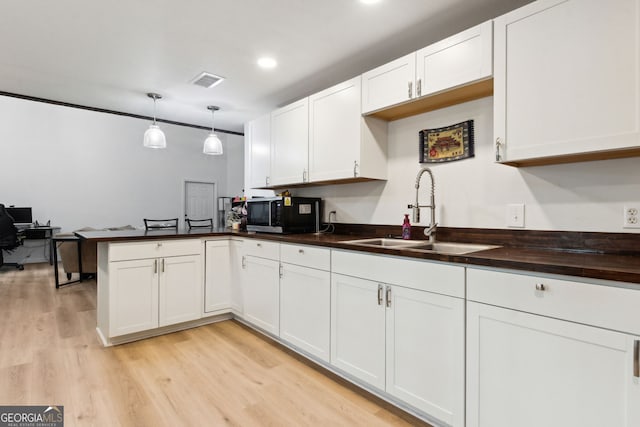 kitchen featuring butcher block countertops, sink, white cabinets, hanging light fixtures, and light hardwood / wood-style floors