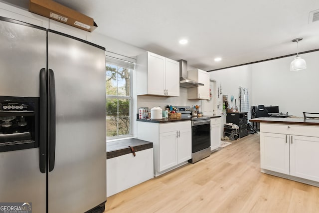 kitchen with wall chimney exhaust hood, hanging light fixtures, light wood-type flooring, appliances with stainless steel finishes, and white cabinets