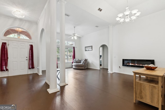 entrance foyer featuring dark wood-type flooring, a towering ceiling, ceiling fan with notable chandelier, and ornate columns