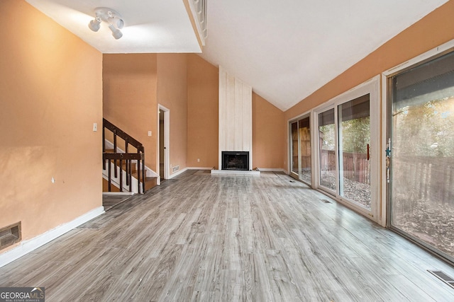 unfurnished living room with vaulted ceiling, light wood-type flooring, and a fireplace