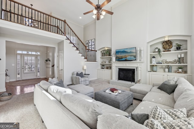 living room featuring a towering ceiling, hardwood / wood-style floors, built in features, a fireplace, and crown molding