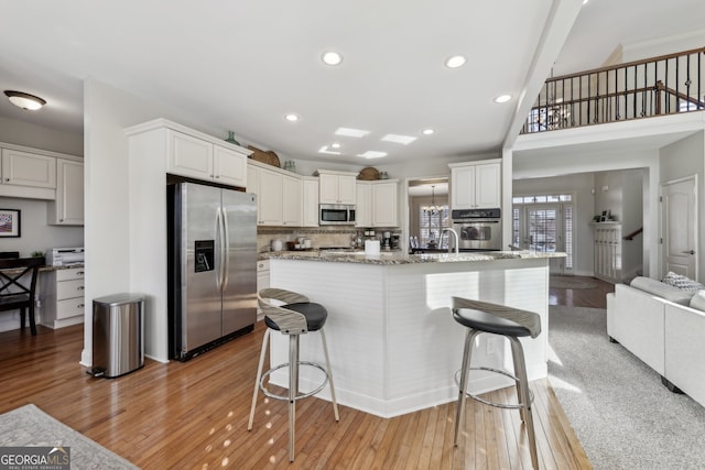 kitchen with stainless steel appliances, a breakfast bar area, white cabinets, and light wood-type flooring