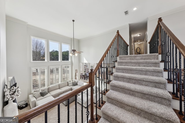 stairs featuring crown molding, ceiling fan, and a towering ceiling