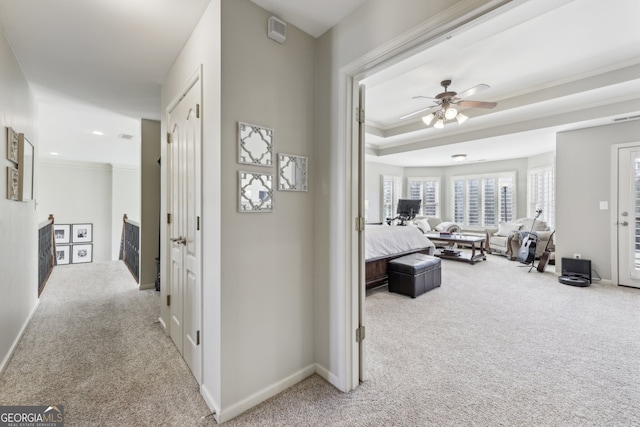 corridor featuring light colored carpet, ornamental molding, and a tray ceiling