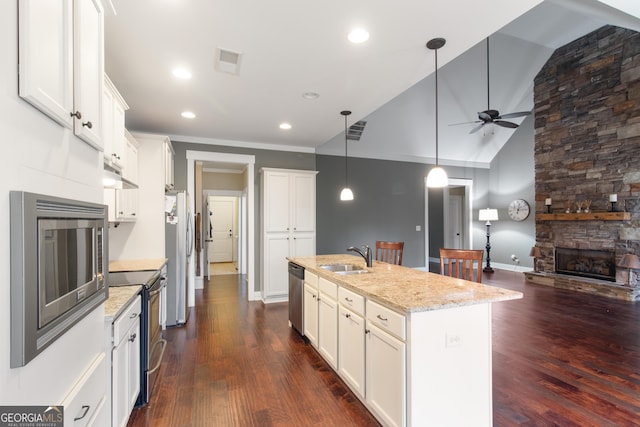 kitchen with appliances with stainless steel finishes, decorative light fixtures, an island with sink, white cabinets, and light stone counters