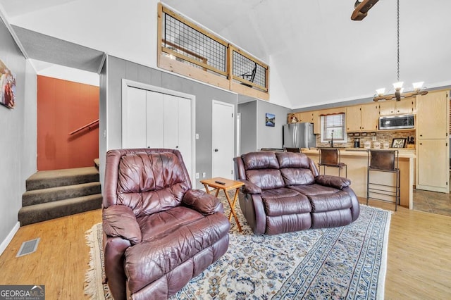 living room with high vaulted ceiling, light wood-type flooring, and a chandelier