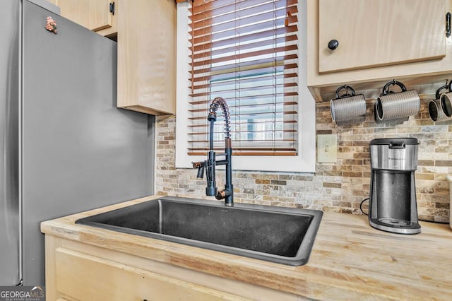 details featuring light brown cabinetry, sink, tasteful backsplash, and stainless steel refrigerator