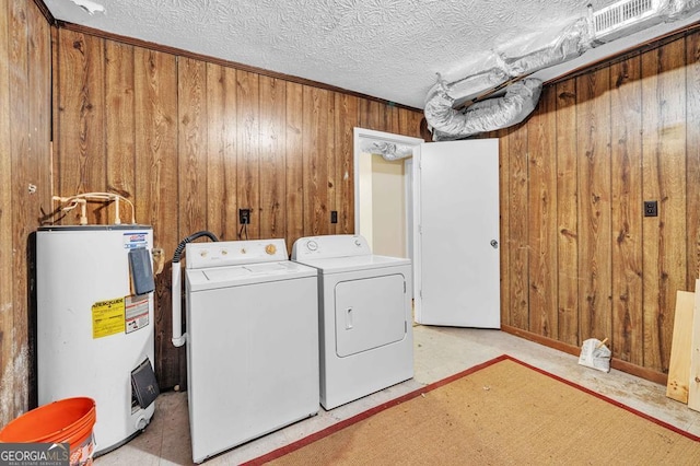 clothes washing area with a textured ceiling, water heater, washing machine and clothes dryer, and wood walls