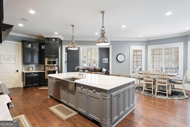 kitchen featuring decorative light fixtures, an island with sink, sink, dark hardwood / wood-style flooring, and stainless steel dishwasher