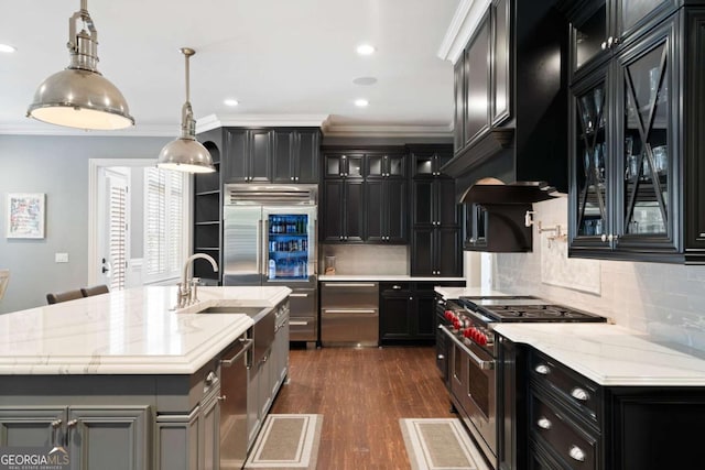 kitchen with pendant lighting, high quality appliances, an island with sink, light stone counters, and crown molding