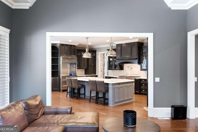 kitchen with ornamental molding, a kitchen breakfast bar, a kitchen island, pendant lighting, and light hardwood / wood-style floors