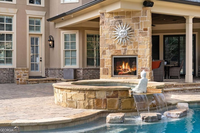 exterior space featuring an in ground hot tub, pool water feature, a large fireplace, and a patio area