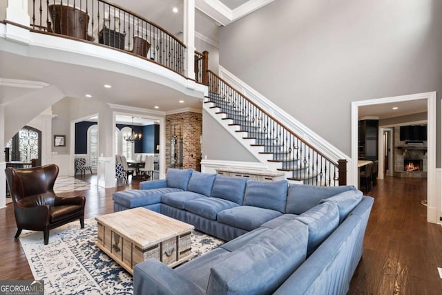 living room featuring dark wood-type flooring, ornamental molding, a chandelier, and a high ceiling