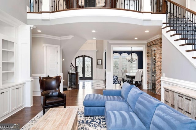 living room with dark wood-type flooring, french doors, crown molding, a notable chandelier, and a towering ceiling