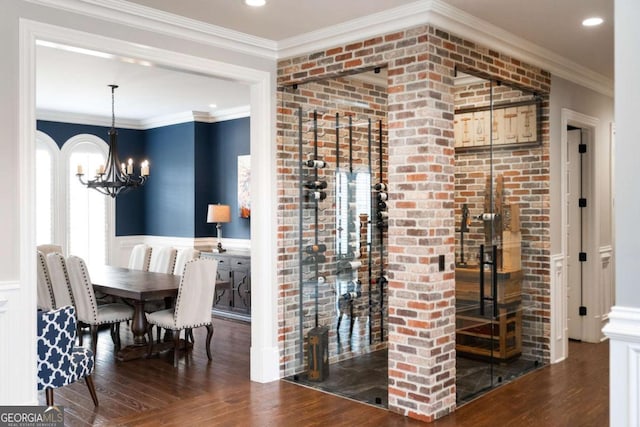 wine area with ornamental molding, dark hardwood / wood-style floors, a chandelier, and brick wall