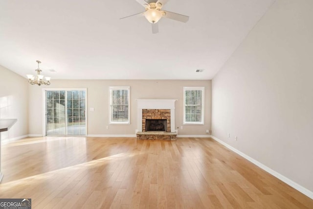 unfurnished living room featuring a stone fireplace, light hardwood / wood-style flooring, and ceiling fan with notable chandelier