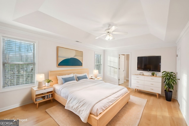 bedroom featuring crown molding, light hardwood / wood-style floors, and a tray ceiling