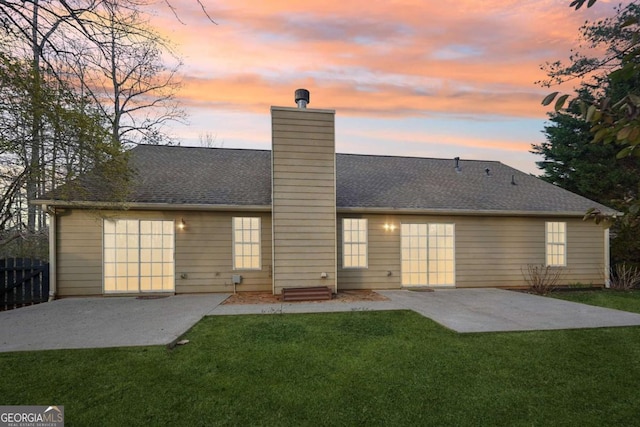 back house at dusk with a lawn and a patio area