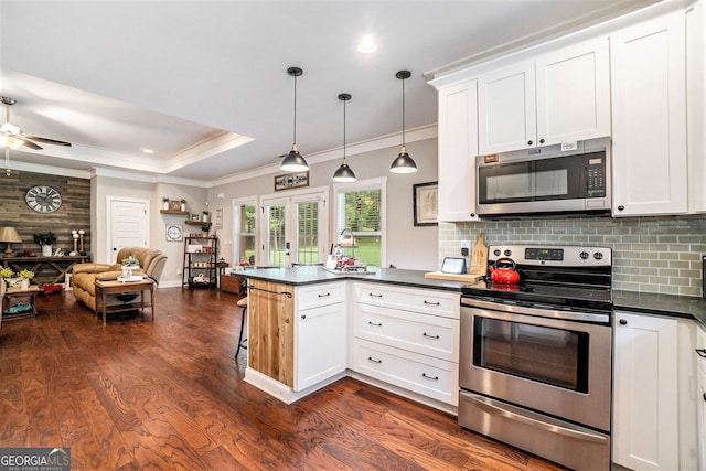 kitchen with pendant lighting, appliances with stainless steel finishes, white cabinetry, a tray ceiling, and kitchen peninsula