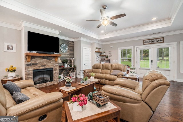 living room with a tray ceiling, ornamental molding, dark hardwood / wood-style flooring, a stone fireplace, and french doors