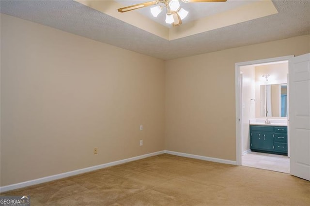 unfurnished bedroom featuring ensuite bathroom, a tray ceiling, light carpet, and a textured ceiling