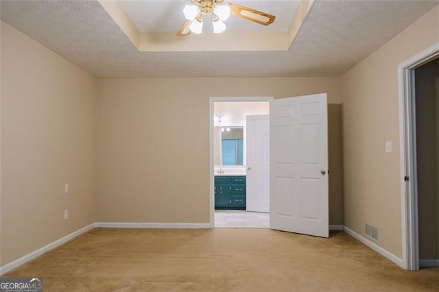 carpeted empty room with ceiling fan, a textured ceiling, and a tray ceiling