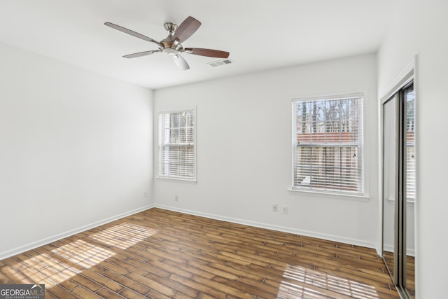 unfurnished bedroom featuring multiple windows, ceiling fan, dark hardwood / wood-style flooring, and a closet