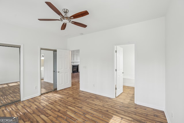 unfurnished bedroom featuring two closets, wood-type flooring, ensuite bath, and ceiling fan