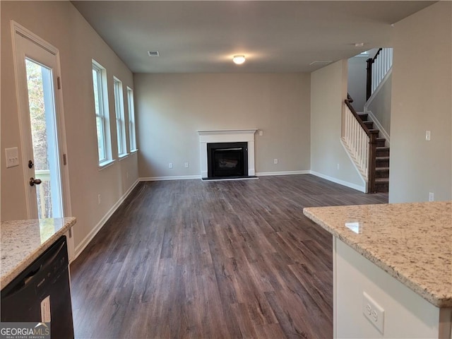 unfurnished living room featuring baseboards, stairway, a fireplace with raised hearth, and dark wood-type flooring