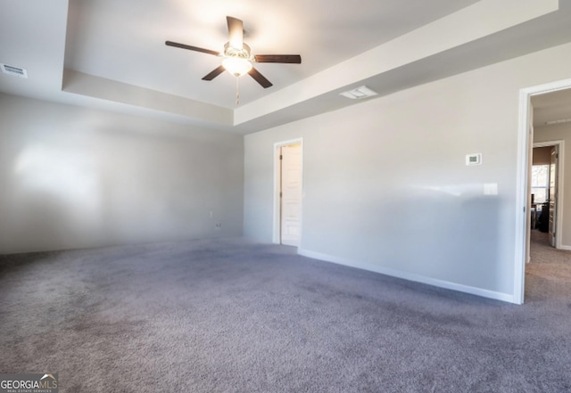 carpeted spare room featuring ceiling fan, a tray ceiling, visible vents, and baseboards