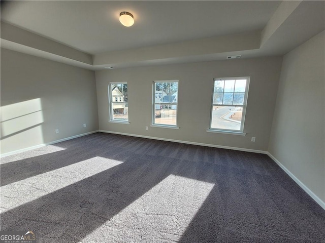 spare room with a raised ceiling, visible vents, dark carpet, and baseboards