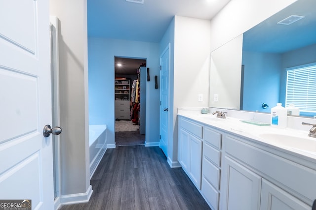 bathroom featuring double vanity, visible vents, a spacious closet, a sink, and wood finished floors