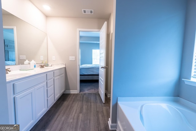 ensuite bathroom with double vanity, visible vents, ensuite bath, wood finished floors, and a sink