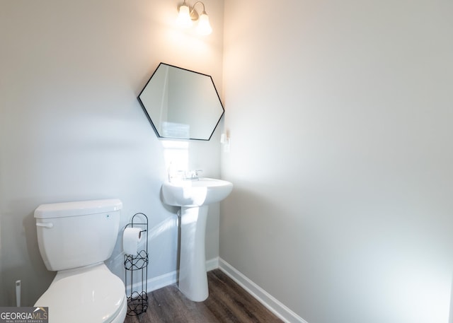 half bath featuring toilet, a sink, baseboards, and wood finished floors