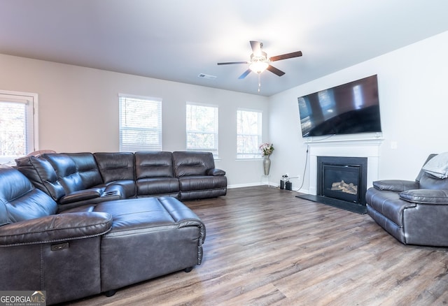 living room with baseboards, visible vents, a ceiling fan, a glass covered fireplace, and wood finished floors