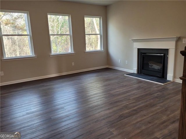 unfurnished living room featuring dark wood-type flooring, a glass covered fireplace, and baseboards