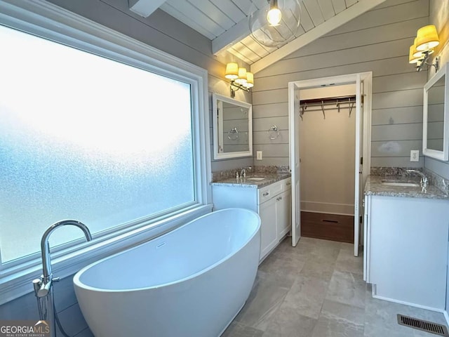 bathroom featuring lofted ceiling with beams, wooden ceiling, vanity, wooden walls, and a bathing tub