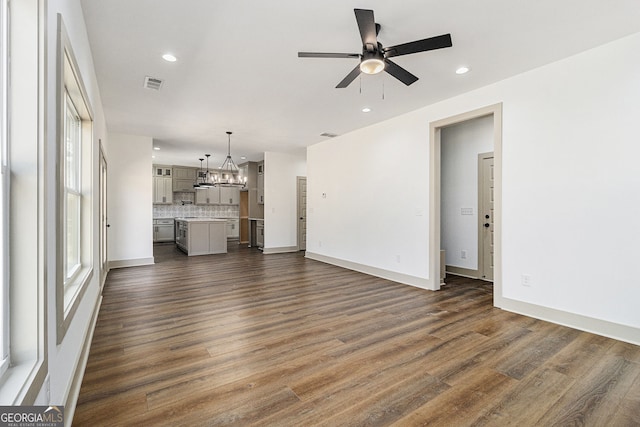unfurnished living room with ceiling fan with notable chandelier and dark hardwood / wood-style flooring