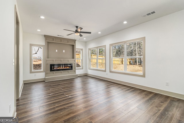 unfurnished living room featuring ceiling fan, a fireplace, dark hardwood / wood-style floors, and a healthy amount of sunlight