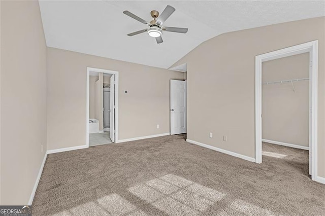 unfurnished bedroom featuring lofted ceiling, ceiling fan, ensuite bathroom, carpet floors, and a walk in closet