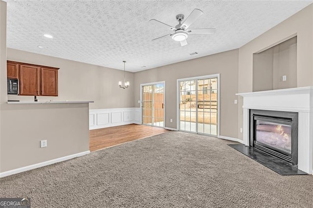 unfurnished living room with dark carpet, ceiling fan with notable chandelier, and a textured ceiling