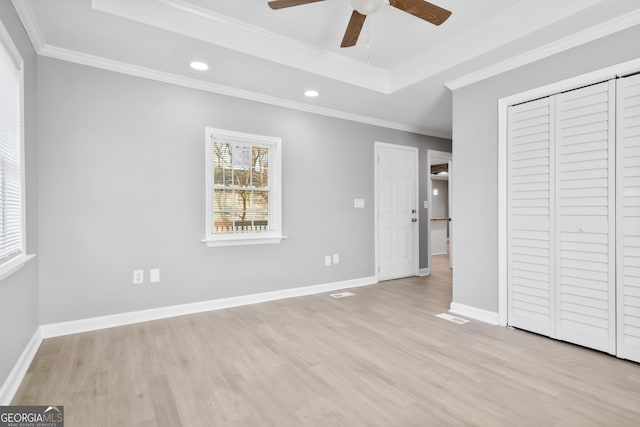 unfurnished bedroom with light hardwood / wood-style floors, a tray ceiling, a closet, ceiling fan, and crown molding