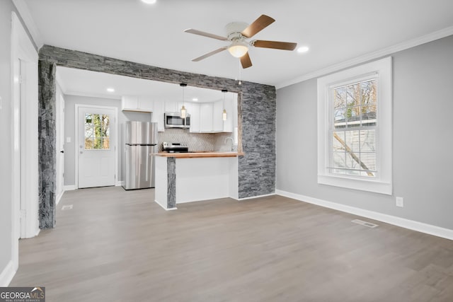 unfurnished living room with ceiling fan, ornamental molding, sink, and light wood-type flooring