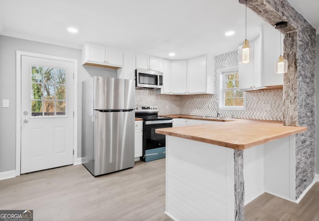 kitchen featuring light wood-type flooring, kitchen peninsula, decorative light fixtures, appliances with stainless steel finishes, and white cabinets